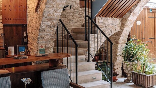 A stone-walled interior with a wooden reception desk, a staircase with black railings, and a seating area with chairs and a table. - Lazaros Stonehouse (Pano Lefkara)