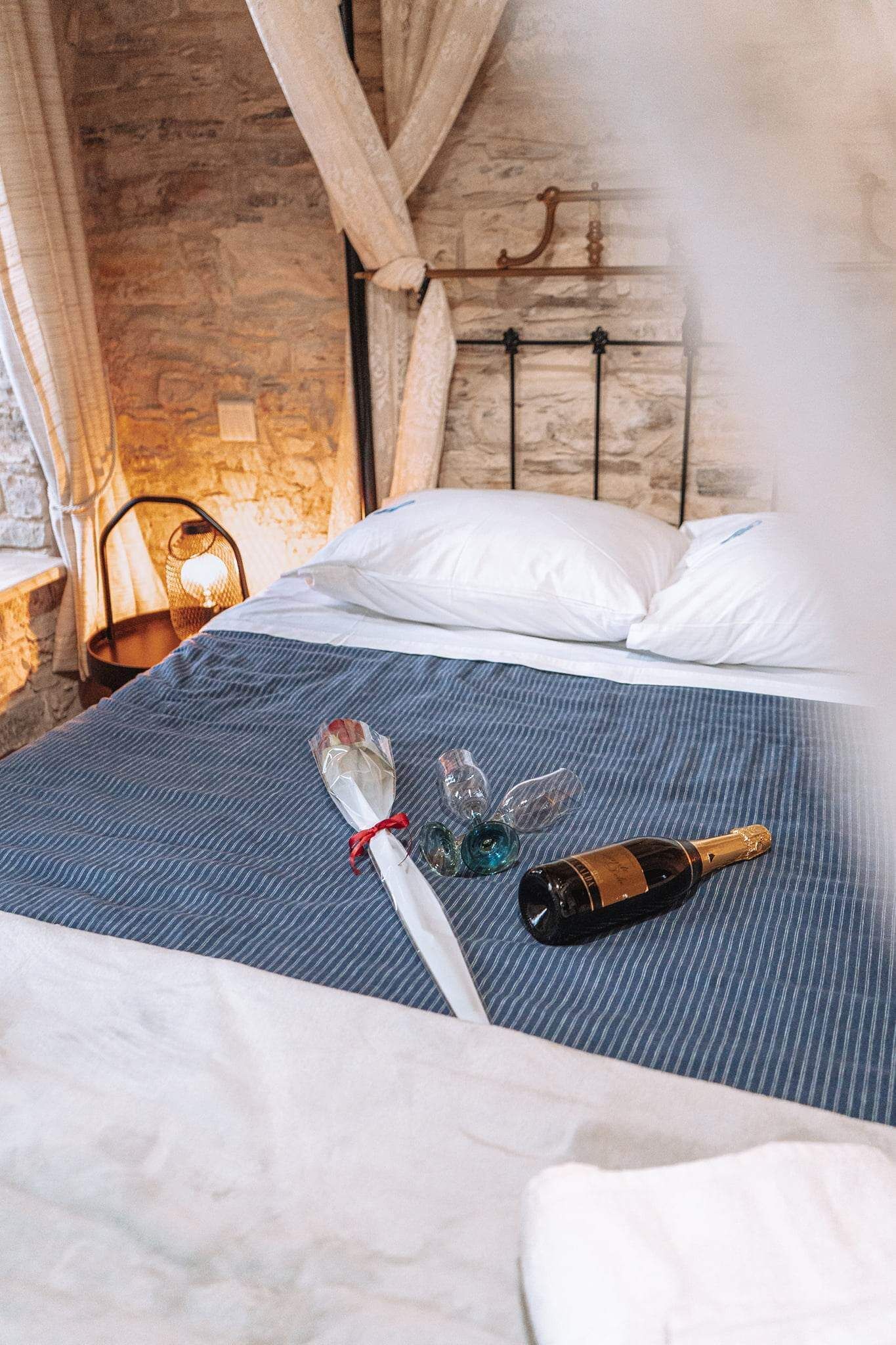 A bed with a blue striped bedspread, a bottle of champagne, and a glass of wine on it.