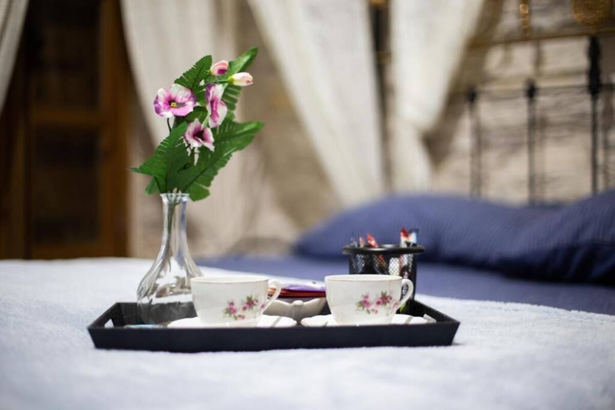 A tray with two floral cups and a vase of flowers on a bed with a blue pillow.