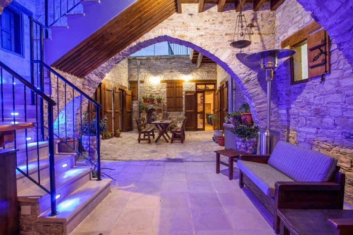A stone-walled courtyard with a wooden staircase, outdoor seating, and a hanging light fixture.