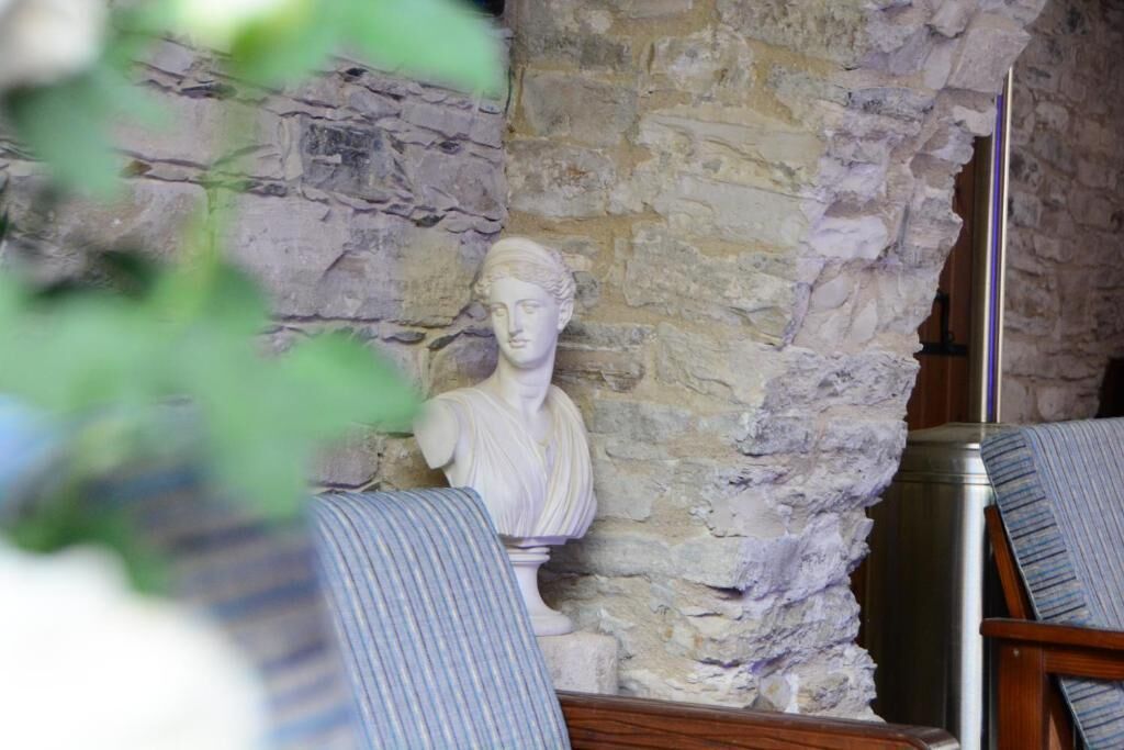A room with a stone wall and a bust sculpture. There are two chairs with striped upholstery.