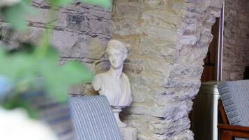 A room with a stone wall and a bust sculpture. There are two chairs with striped upholstery.