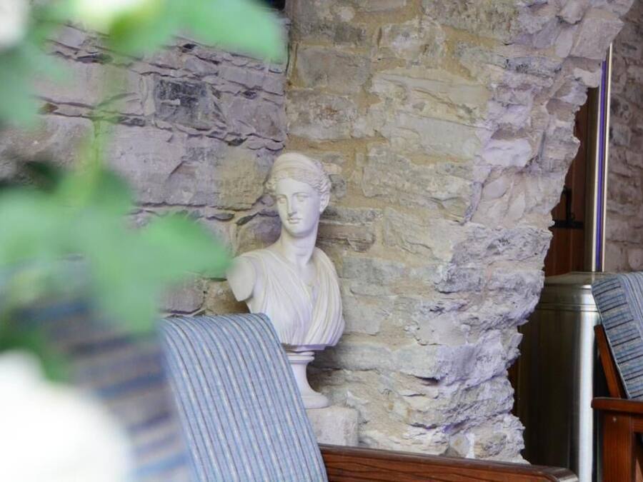 A room with a stone wall and a bust sculpture. There are two chairs with striped upholstery.