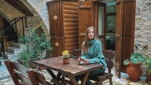 A rustic wooden table and chairs set in a stone courtyard with a wooden cabin and a stone wall in the background. - Lazaros Stonehouse (Pano Lefkara)