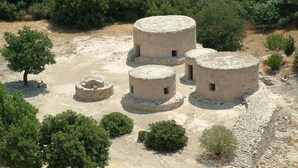 A historical site with three round stone structures surrounded by trees and a stone wall. - Lazaros Stonehouse (Pano Lefkara)