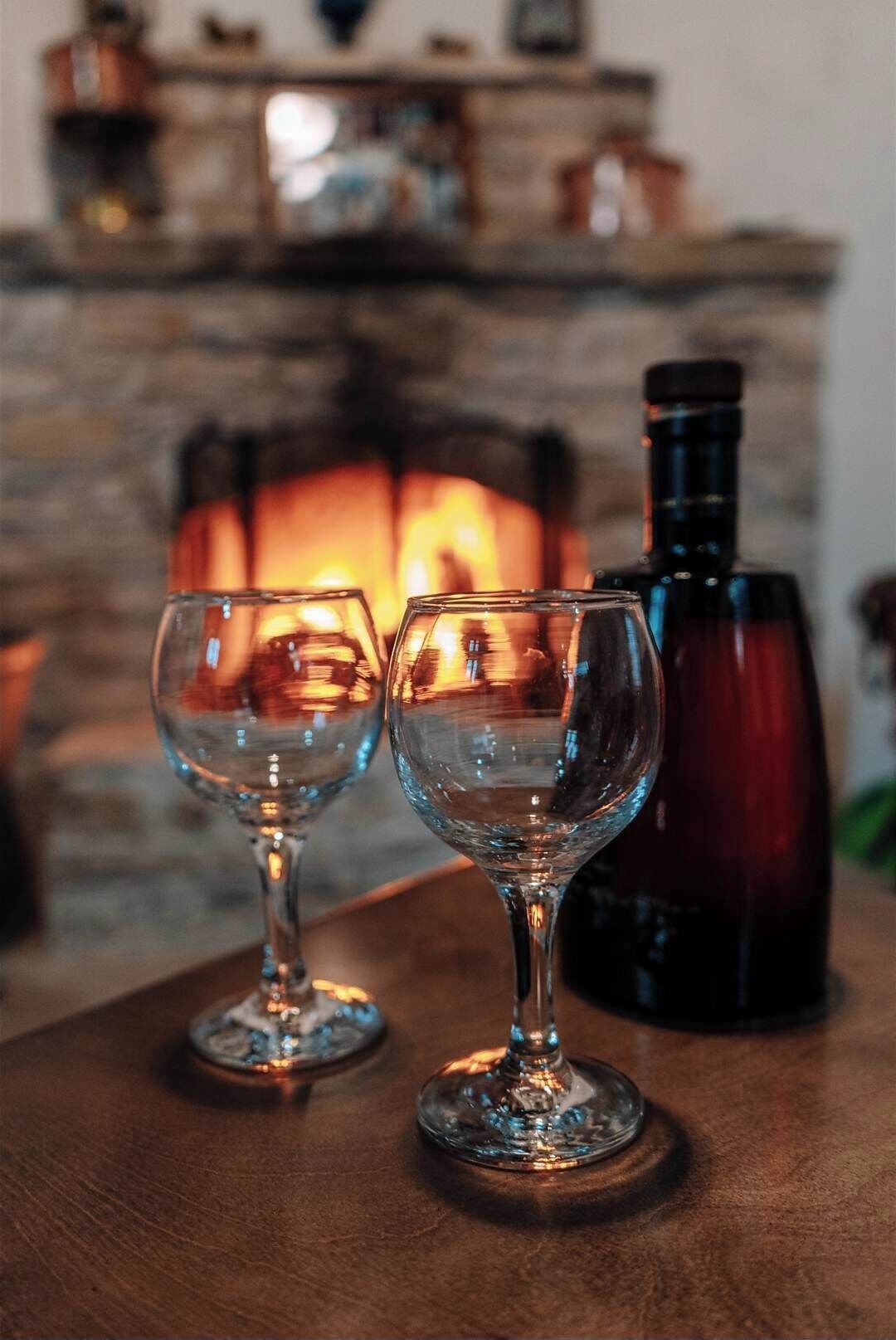 Due bicchieri da vino vuoti su un tavolo di legno, con un camino sullo sfondo.