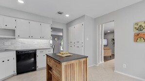 Une cuisine moderne avec des meubles blancs, un lave-vaisselle noir et un îlot central en bois.