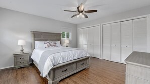 Une chambre à coucher comprenant un lit, des tables de chevet, un ventilateur de plafond et un dressing.