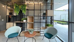 Un interior moderno con dos sillas, una mesa, un separador de vidrio con estantes y vistas al exterior.