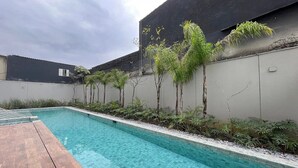 Una piscina con cubierta de madera, rodeada de plantas y un muro bajo.