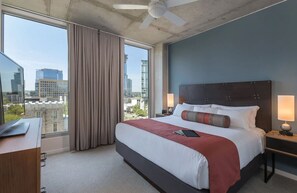 A hotel room with a large bed, a desk, and a view of the cityscape.
