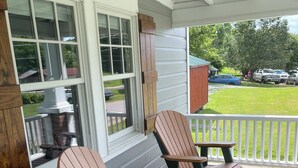 A covered porch with Adirondack chairs and a table, white siding, and a view of the backyard. - Recently updated Park Street Cottage with garage in Downtown Greeneville, TN. (Greeneville)