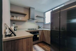 Une cuisine moderne avec des meubles en bois, un réfrigérateur en acier inoxydable, un four encastré et une machine à café.