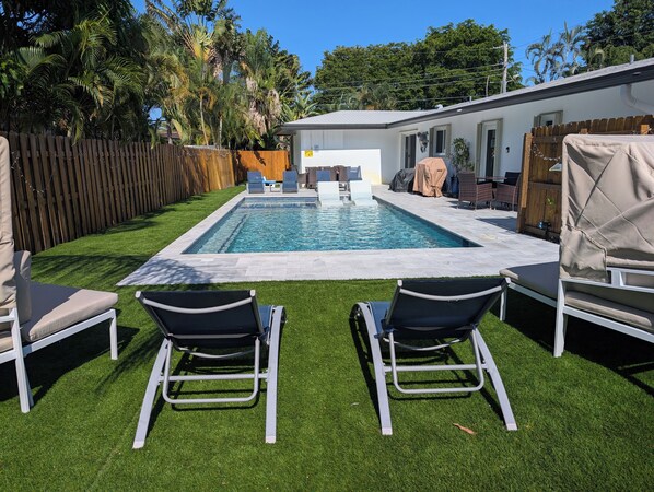 A rectangular swimming pool with a tiled deck, surrounded by artificial grass and two lounge chairs. - Fun-tastic Oasis! Shared Heated Pool n Spa! Beach 1.4 mi! Walkable Food n Fun! (Fort Lauderdale)