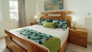 Un dormitorio con cama de madera, ropa de cama estampada en verde y blanco, dos lámparas de noche y una ventana con cortinas.