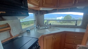 A compact RV kitchen with a stove, microwave, and sink.