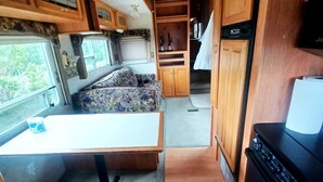 A compact RV kitchen with wooden cabinets, a stove, and a ceiling fan.