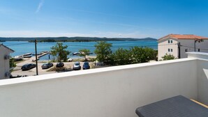 A balcony with a view of a lake, parked cars, and a building with a tiled roof. - Awesome apartment in Turanj with WiFi (Turanj)