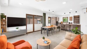 A modern living room with a TV, orange sofas, a coffee table, and a dining area with a kitchen in the background. - Lovely home in Kadumi (Kadumi)