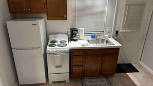 Une cuisine de taille réduite, équipée d’un réfrigérateur, d’une cuisinière, d’un évier et de meubles de rangement en bois.