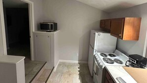 Une cuisine de taille réduite, avec des meubles blancs, une cuisinière, un four à micro-ondes et un réfrigérateur.
