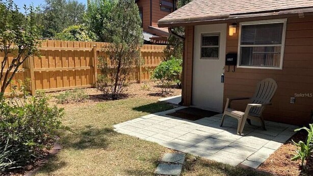 Un jardin arrière aménagé dans une propriété résidentielle, avec une terrasse dallée, une clôture en bois et un petit espace dédié au jardinage.