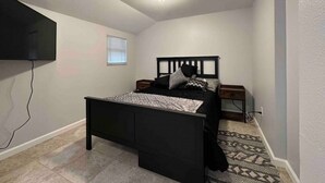 Une chambre à coucher avec un lit, des tables de chevet, un téléviseur fixé au mur et un tapis à motifs.