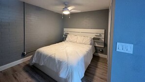 Un dormitorio con cama, ventilador de techo, mesita de noche y toma de corriente.