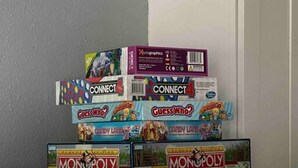 Una pila de juegos de mesa como Connect 4, Guess Who? y Monopoly en un estante.