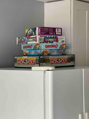 En hög med brädspel, inklusive Connect 4, Gissa vem? och Monopol, står på en hylla.