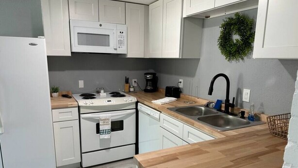 Una cocina moderna con armarios blancos, microondas, estufa, lavavajillas, pileta y encimera de madera.