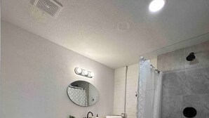 Un baño con inodoro, lavamanos, espejo, ducha y una alfombra.