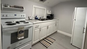 Une cuisine avec des meubles blancs, une cuisinière, un réfrigérateur et une fenêtre avec des stores.