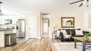 A modern kitchen with stainless steel appliances, a wooden floor, and a dining area with a black sofa and a coffee table. - The Clemson Cottage - 3.6 mi. to Memorial Stadium (Seneca)