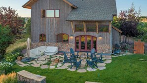 A wooden house with a stone foundation, a patio with outdoor seating, and a fenced yard. - HUGE VIEWS + LUX Finishes Outside Aspen (Basalt)