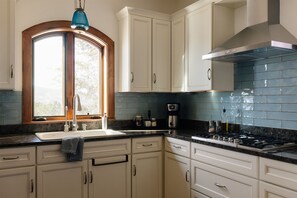 A kitchen with white cabinets, a black countertop, a window with a wooden frame, and a blue backsplash.