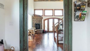 A spacious room with a wooden floor, a patterned rug, a stone fireplace, and a view of a staircase leading to another level. - HUGE VIEWS + LUX Finishes Outside Aspen (Basalt)