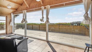 A wooden interior with large windows overlooking a wooden deck and a view of houses. - Stunning home in Vinderup with kitchen (Vinderup)