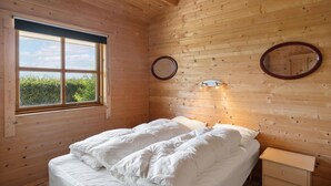 A wooden cabin bedroom with a bed, a nightstand, a mirror, and a window with a view of greenery. - Stunning home in Vinderup with kitchen (Vinderup)