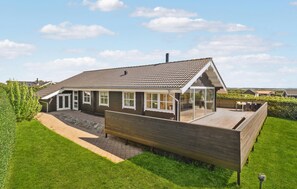 Ein zweistöckiges Haus mit einer großen Terrasse, einer überdachten Veranda und Blick auf die umliegende Landschaft.