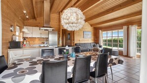 A modern kitchen with wooden walls, a dining area with a patterned tablecloth, and a large window with curtains. - Stunning home in Vinderup with kitchen (Vinderup)