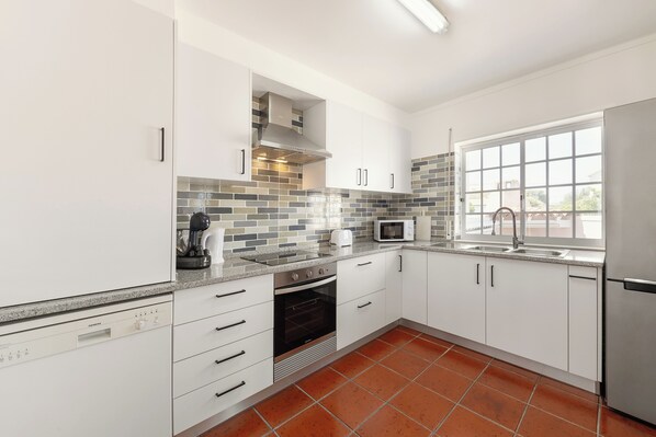 A modern kitchen with white cabinets, a stainless steel refrigerator, a built-in oven, and a microwave.