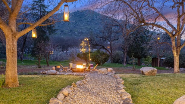 A gravel path leading to a fire pit with seating, surrounded by trees and lanterns.