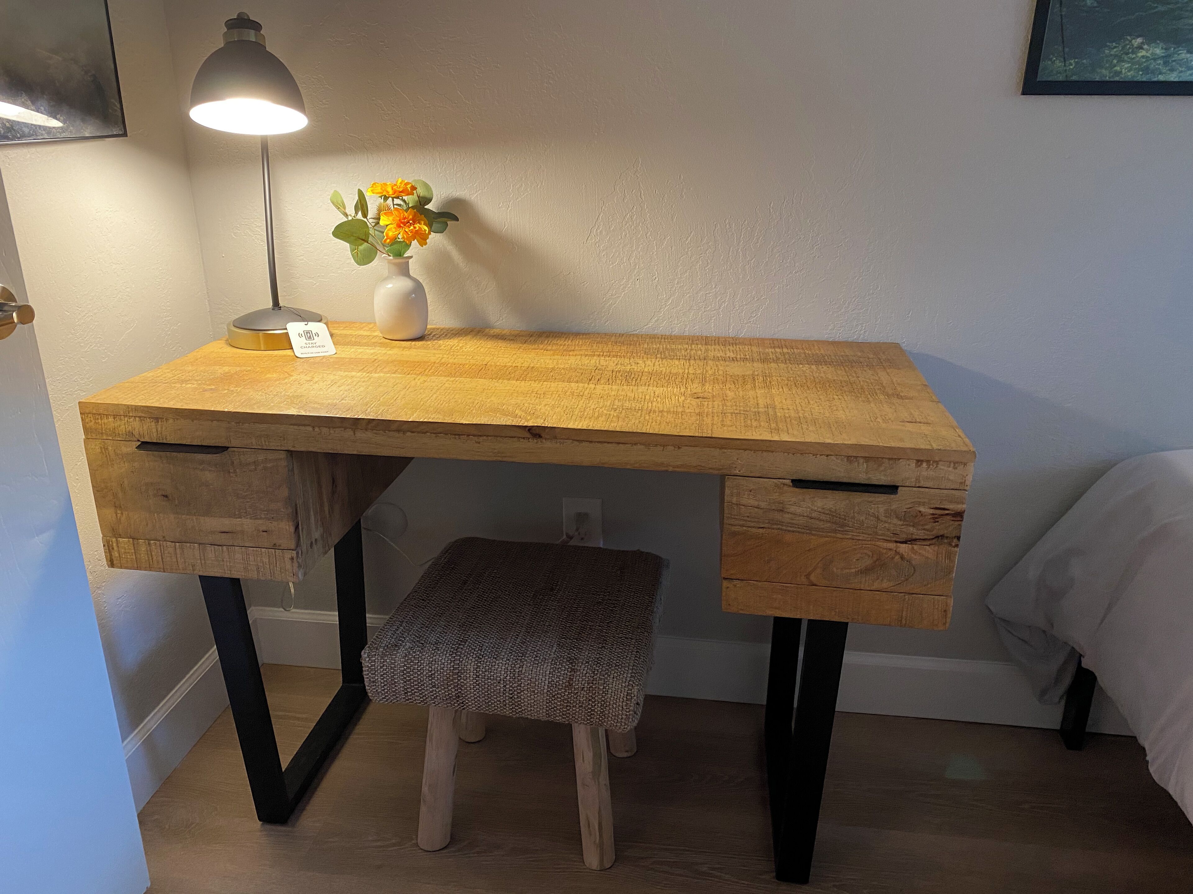 A wooden desk with a lamp, a vase with flowers, and a bench.