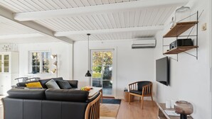 Ein modernes Wohnzimmer mit einem schwarzen Ledersofa, einem Holznachttisch und einem an der Wand befestigten Fernseher.