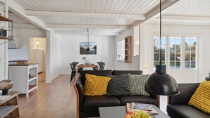 Ein modernes Wohnzimmer mit einem schwarzen Ledersofa, einem Holztisch und einem Essbereich im Hintergrund.