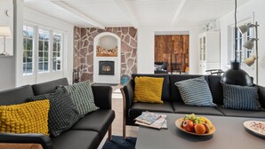 Ein modernes Wohnzimmer mit Kamin, schwarzen Ledersofas und einem Esstisch mit Obst.