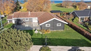 Ein zweistöckiges Haus mit geneigtem Dach, einem umzäunten Garten und Blick auf das Meer.