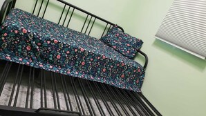 Ein Bett mit floralem Überwurf und passendem Kopfkissen, einem Metallgestell und einem Fenster mit Jalousien.