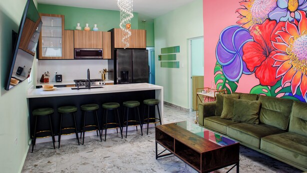 Eine moderne Küche mit Bar, einem grünen Sofa und einem farbenfrohen Blumenwandbild.